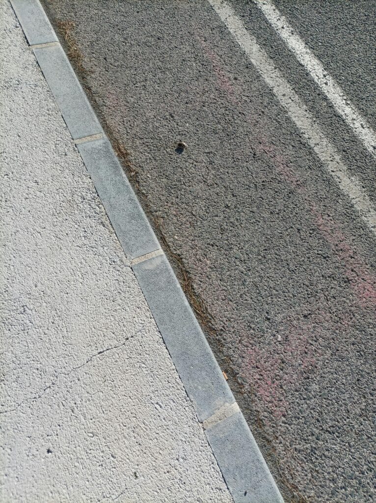 High angle view of an urban street curb showing asphalt and concrete textures.