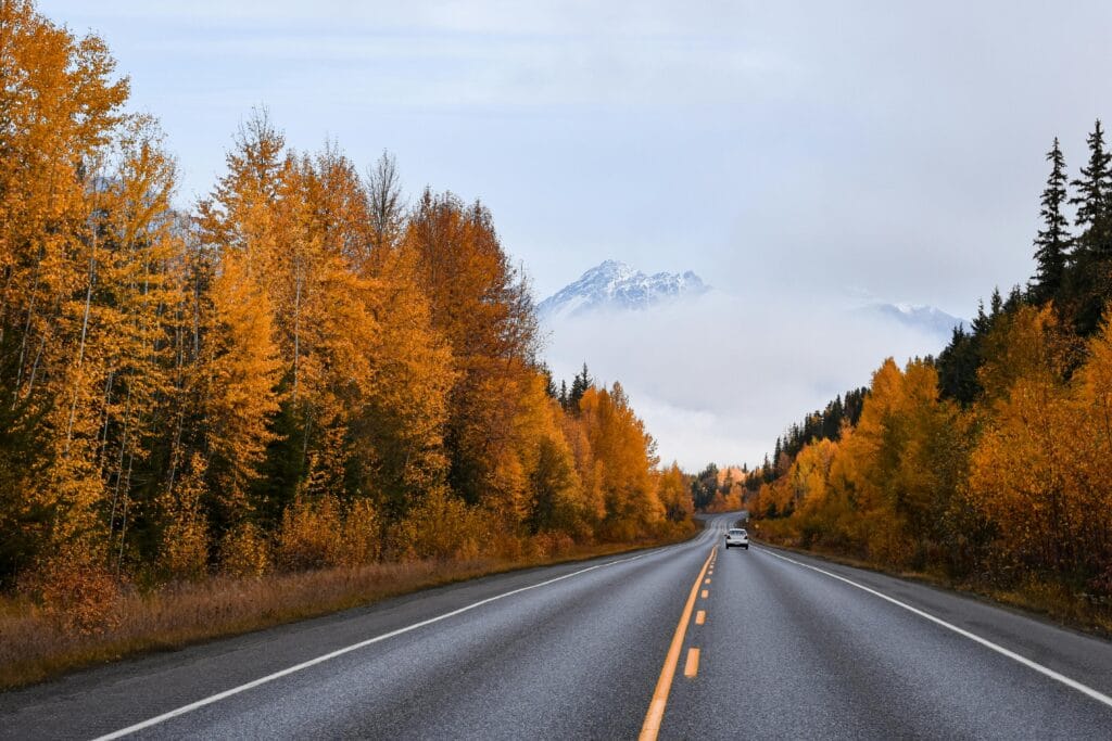 Panoramic view of a highway amidst vibrant autumn foliage and misty mountains in Terrace, Canada.